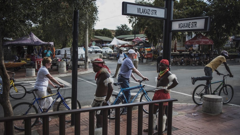 Traditional dancers stand idle as a couple of Dutch tourists and their guide push their bicycle past the Mandela House Museum in Vilakazi Street in Soweto, Johannesburg.