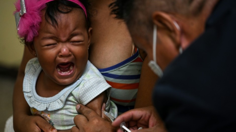 A girl accompanied by her mother receives a dose of measles and rubella vaccine from medical personnel at a community health center in the Lidice neighborhood in Caracas