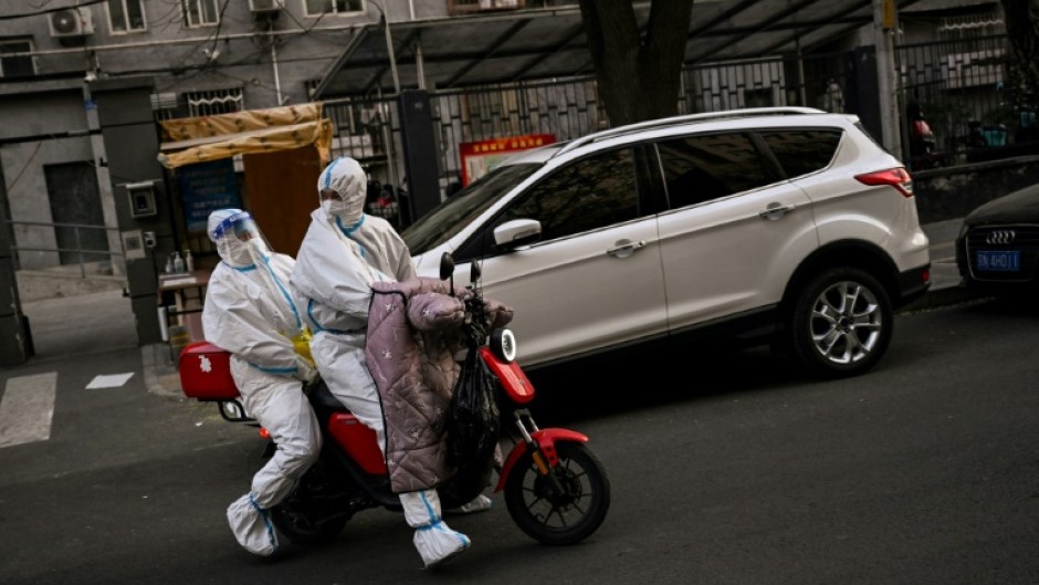 Health workers wearing protective equipment (PPE) ride a scooter near a residential area under lockdown