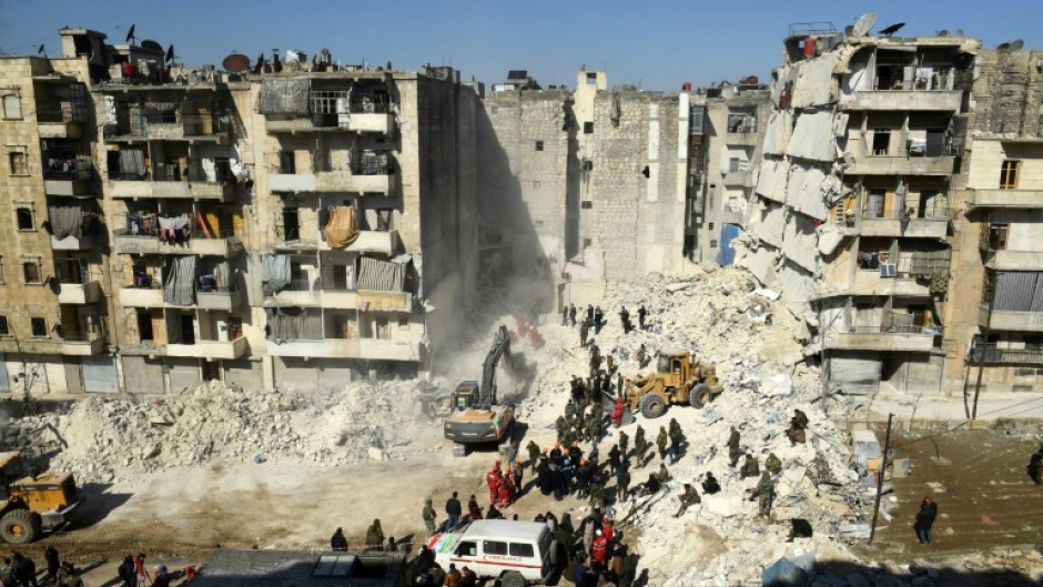 Syrian soldiers look on as rescuers use heavy machinery sift through the rubble of a collapsed building in the northern city of Aleppo