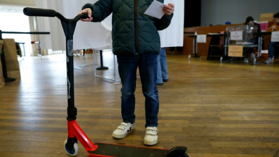 A voter with a ballot and an e-scooter inside a voting station in Paris' 17th Arrondissement