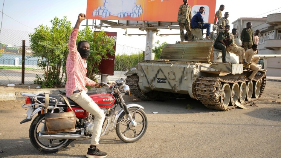 A man raises his arm in support as he drives near Sudanese army soldiers loyal to army chief Abdel Fattah al-Burhan in the Red Sea city of Port Sudan on April 20