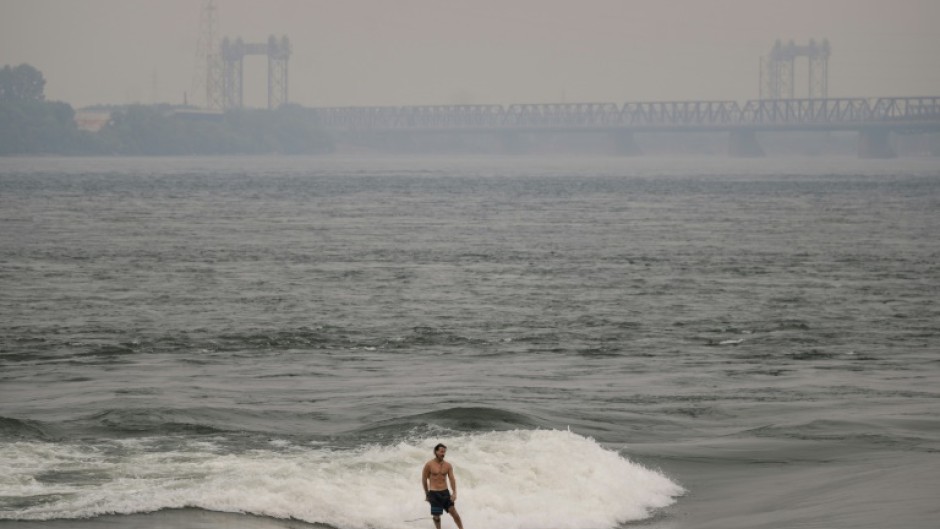 A man surfs in the St. Lawrence river with smoke caused by wildfires in northern Quebec in the background in Montreal, Canada on June 25, 2023