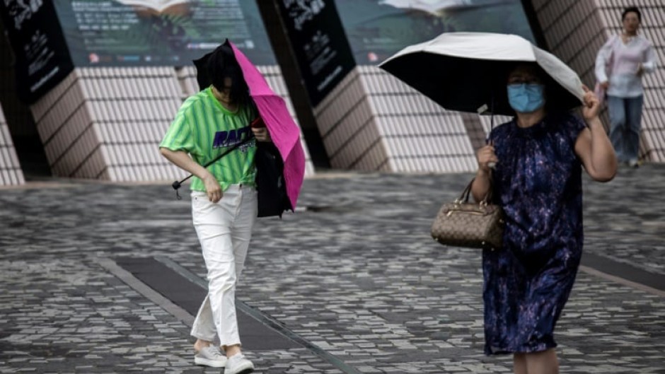 People holding tightly to umbrellas walk near Victoria Harbour as Typhoon Talim passes near Hong Kong on July 17, 2023