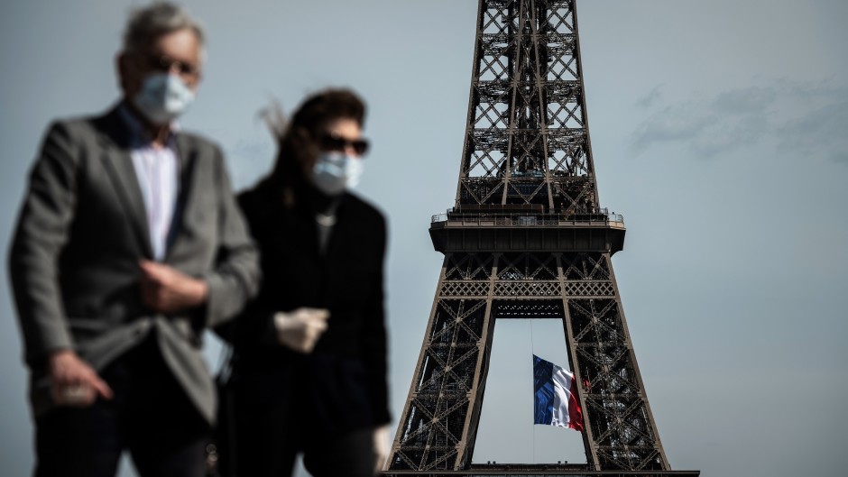 A man and a woman wearing face masks walk on Trocadero Plaza as a French national flag flies on the Eiffel Tower in Paris.