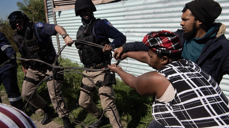 Members of the Cape Town Metro Police try to pull away a piece of illegally connected electricity wire from residents of an informal settlement called Oasis Farm, near Cape Town, on September 13, 2023.