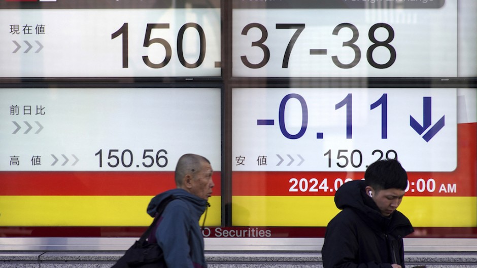 People walk past an electronic board showing the rate of the Japanese yen. AFP/Kazuhiro Nogi