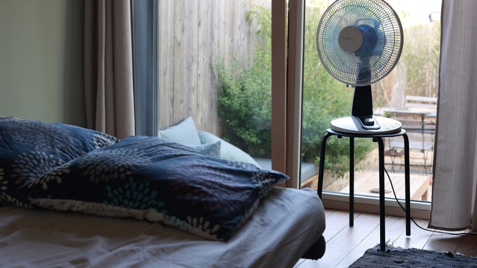 File: A fan next to a bed in a room. 