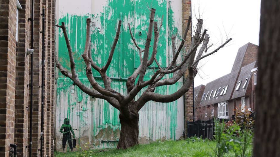 A stencil of a person having spray painted tree foliage onto a wall behind a leafless tree, a graffiti artwork confirmed as being the work of Banksy. AFP/Adrian Dennis