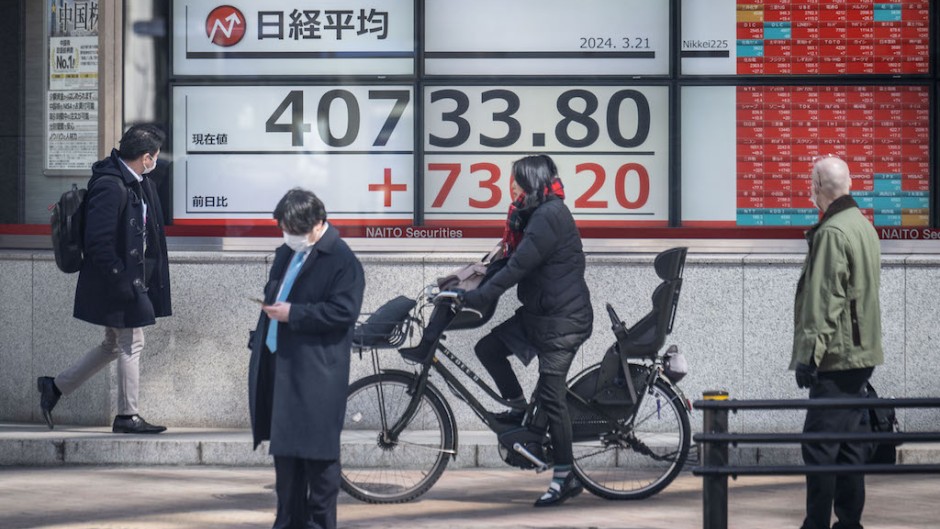People walk past an electronic board showing a share price of the Nikkei index of the Tokyo Stock Exchange. AFP/Yuichi Yamazaki