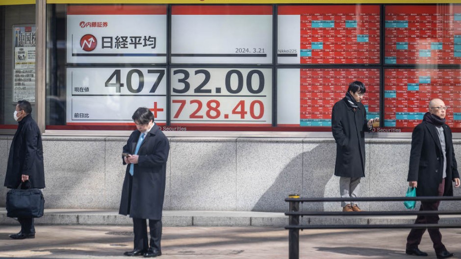 People check their phones next to an electronic board showing a share price of the Nikkei index of the Tokyo Stock Exchange in Tokyo. AFP/Yuichi Yamazaki