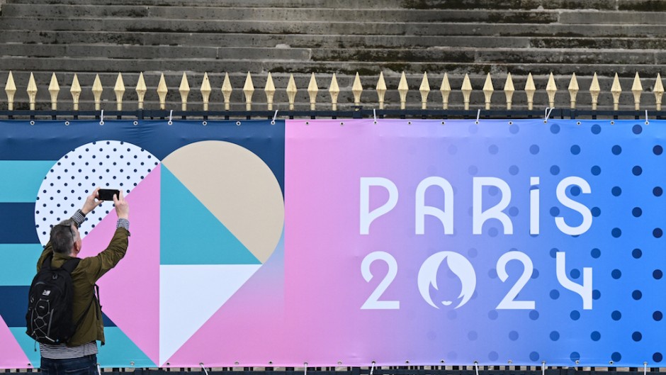 A bystander uses a smartphone to take an image of a banner for the forthcoming Paris 2024 Olympic Games. AFP/Stefano Rellandini