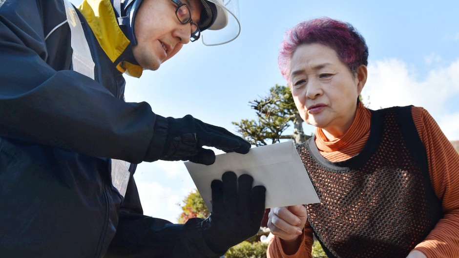 File: A postal delivery person hands an envelope containing a notification card for the My Number common identification system to a woman in Sunagawa. AFP/Kenji Shimizu/Yomiuri