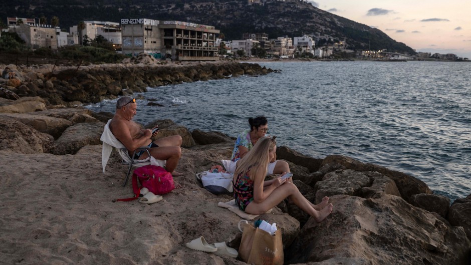 People sit on the rocks by the Mediterranean sea in Israel's northern coastal city of Haifa. AFP/Menahem Kahana