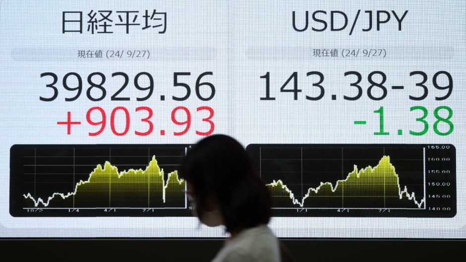 A pedestrian walks past an electronic board showing the closing numbers on the Tokyo Stock Exchange. AFP/JiJi Press