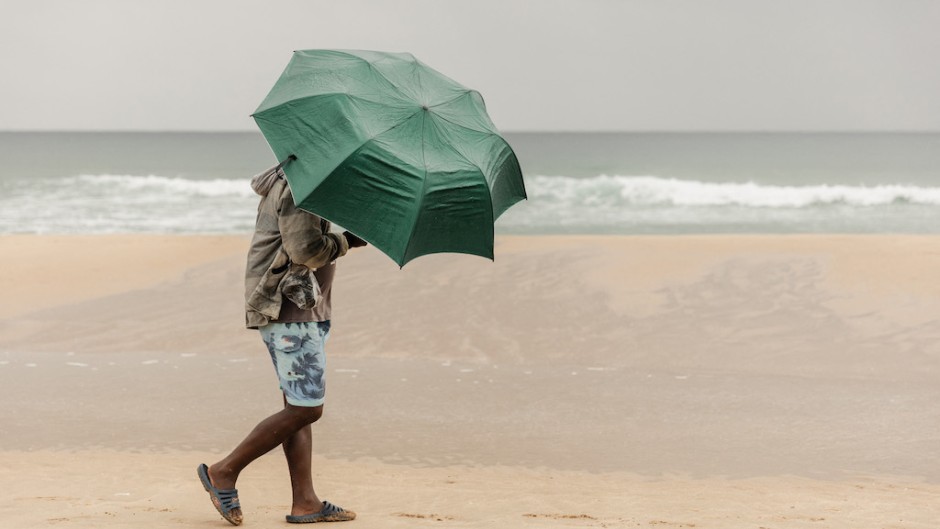 File: A beachgoer uses an umbrella to protect himself against the rain in Durban. AFP/Rajesh Jantilal
