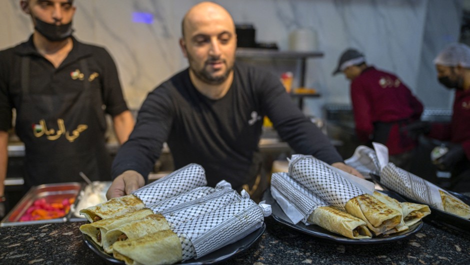 A waiter serves Gaza-style turkey shawarma sandwiches, wrapped in paper with the Kefiyeh pattern, at the 'Hay Al-Rimal' Palestinian-owned restaurant in Cairo. AFP/Khaled Desouki