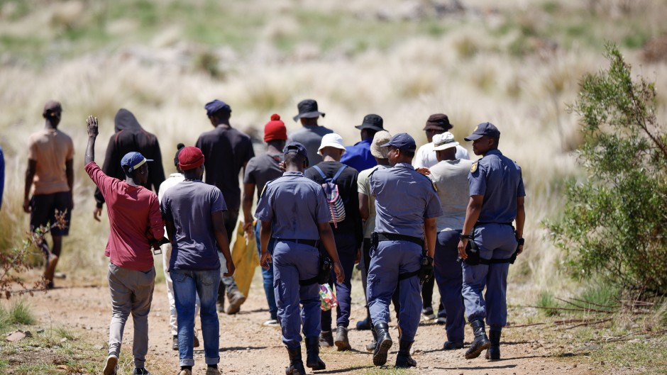 Police officers escort volunteers and community members to an opening to the mine shaft in Stilfontein. AFP/Phill Magakoe