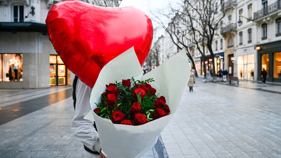 A man holds a bouquet of red roses and a red heart shaped balloon as a Valentine s Day gift. Matthieu Delaty/Hans Lucas via AFP
