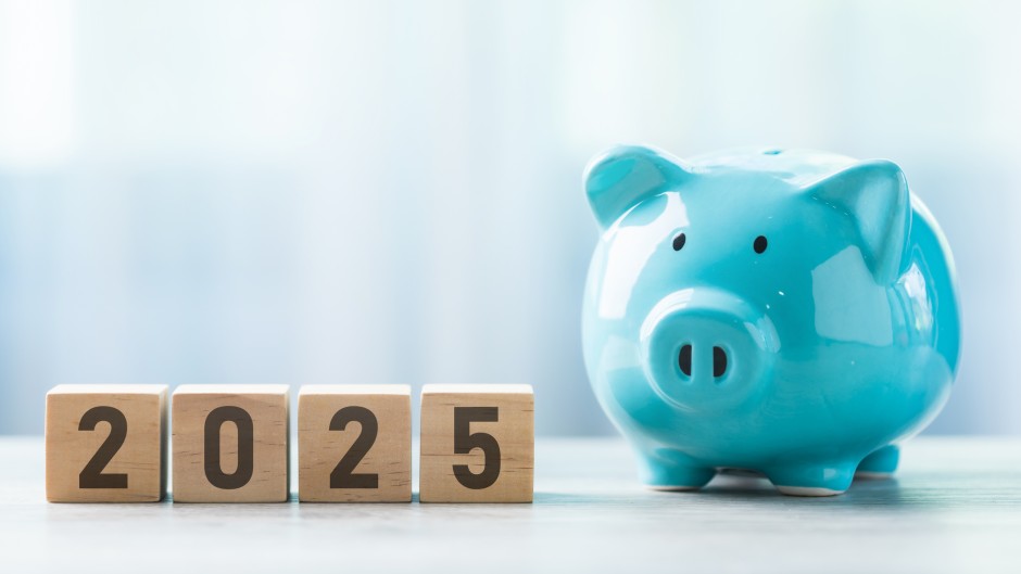 File: 2025 written on a wooden block beside a blue piggy bank. GettyImages/PhanuwatNandee