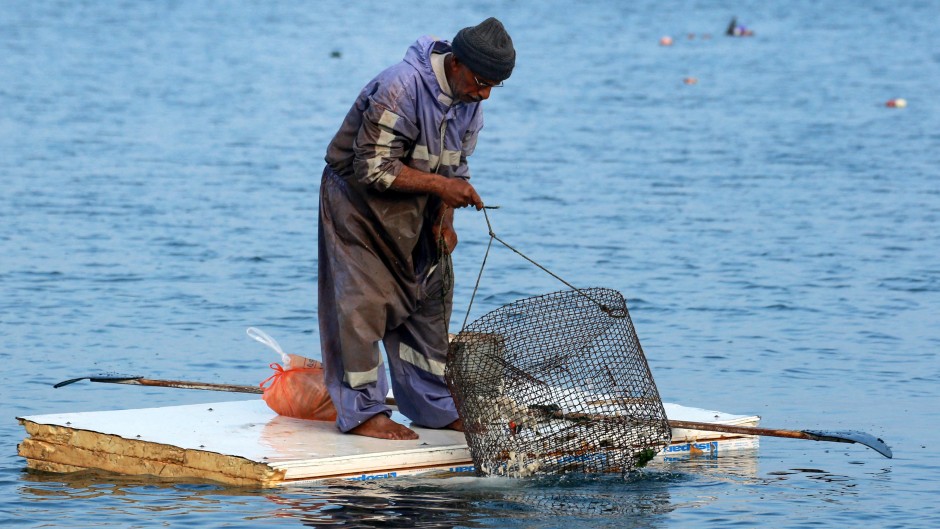 A Palestinian man stands on the door of a refrigerator that he uses as a makeshift rowing boat. AFP/Bashar Taleb