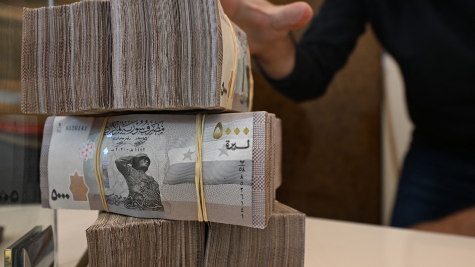 An employee at a currency exchange shop stacks Syrian bills at a shop in Damascus. AFP/Louai Beshara