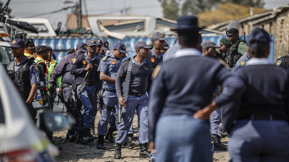 South African Police Service (SAPS) officers walk during raid to retrieve looted goods during a protest at Diepkloof Hostel in Soweto on May 19, 2025. 