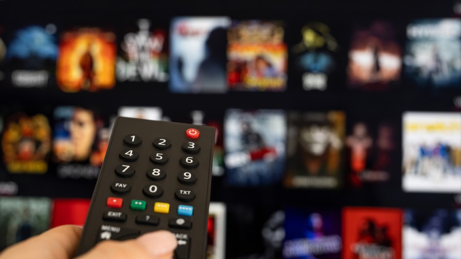 File: A woman holding a TV remote with streaming services in the background. GettyImages/bymuratdeniz