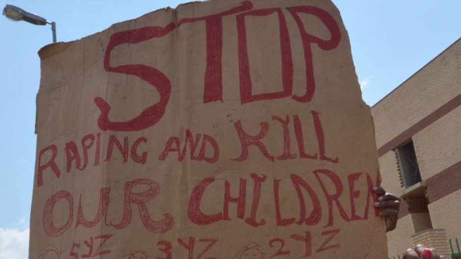File: A protester holds a placard reading "Stop Raping and Kill(ing) our Children". AFP/Alexander Joe