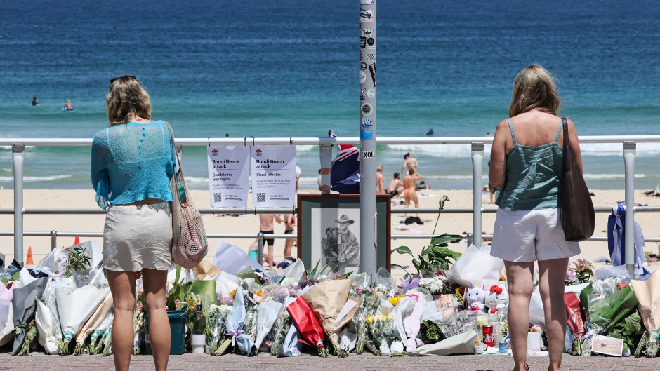 People stand in front floral tributes left at the promenade of Bondi Beach in Sydney. AFP/David Gray