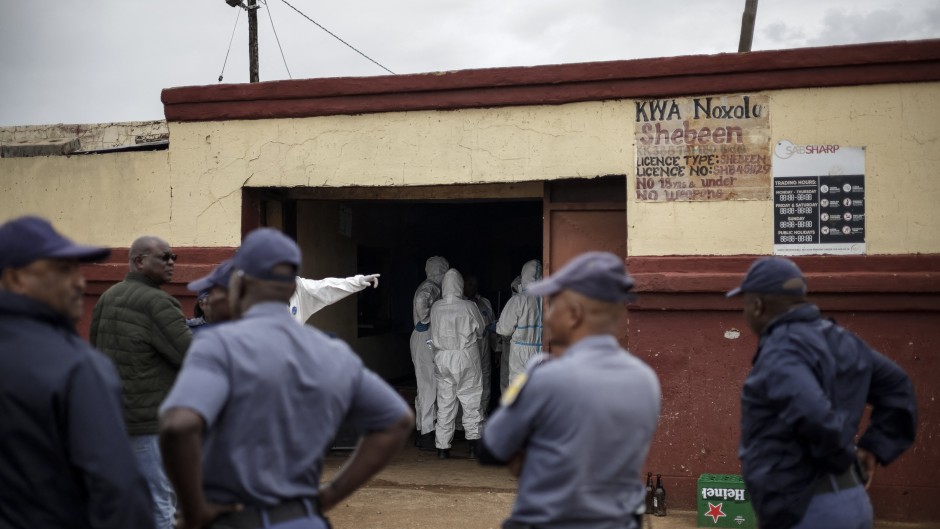 Police officers watch as SAPS Forensic Pathology Services members work at the scene of the Bekkersdal tavern attack. AFP/Emmanuel Croset
