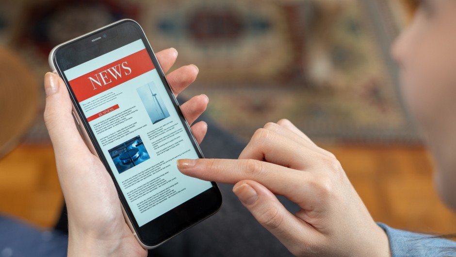 File: A woman reading the news on a phone. GettyImages/izzetugutmen