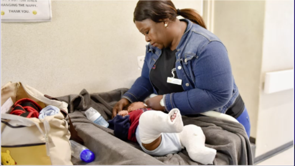 Baby with two casts on their legs being attended by a nurse