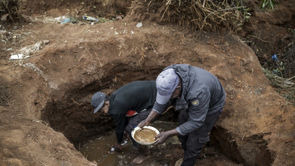 Artisanal miners pan for gold in a hold dug in a patch of land where artisanal miners look for gold outside Springs, Ekurhuleni, on February 15, 2026.