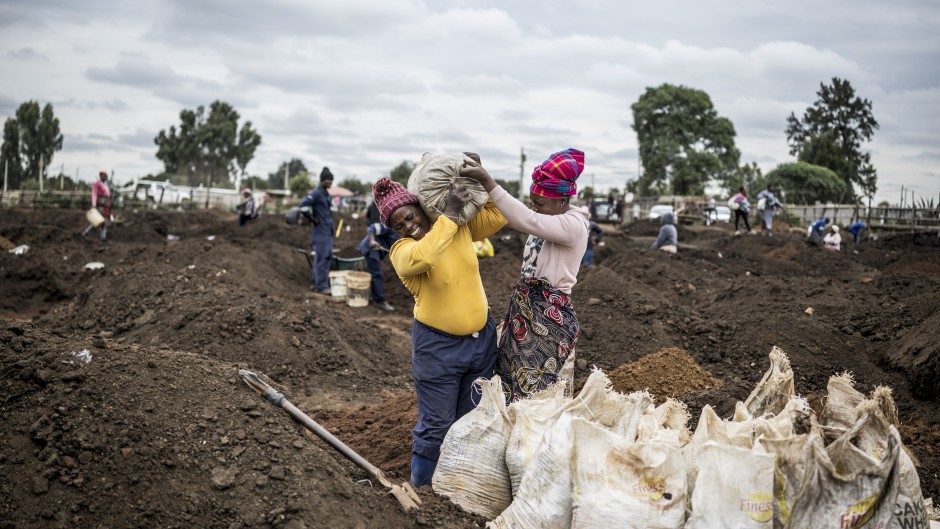 A woman grimaces as she is helped to load a sack of soil on her shoulder in a patch of land where artisanal miners look for gold outside Springs, Ekurhuleni, on February 15, 2026.