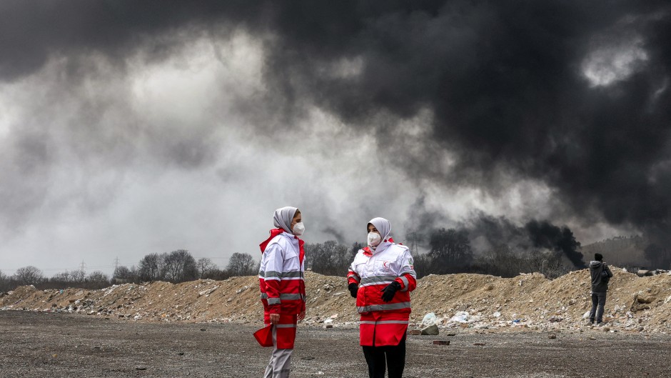 Members of Iran's Red Crescent society stand near smoke plumes from an ongoing fire following an overnight airstrike on the Shahran oil refinery in northwestern Tehran. AFP