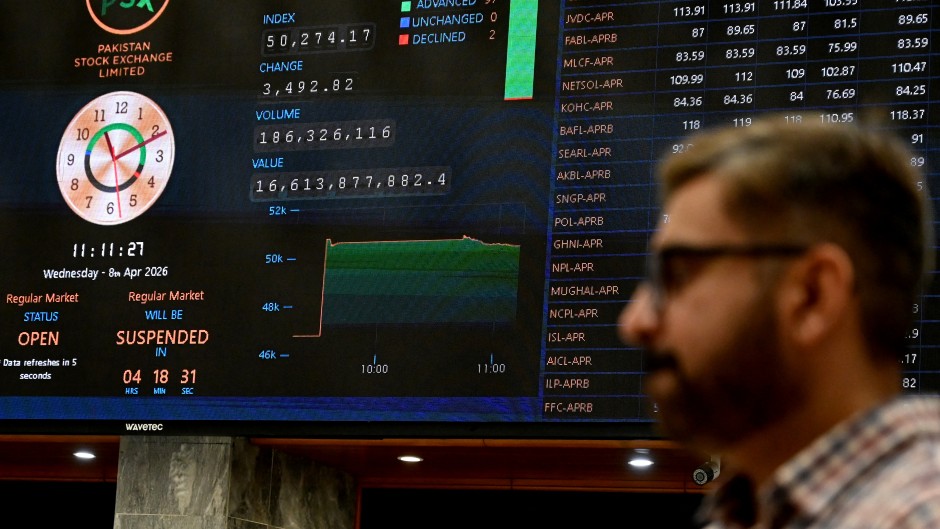 A stockbroker walks past share prices on a digital board during a trading session at the Pakistan Stock Exchange. AFP/Rizwan Tabassum