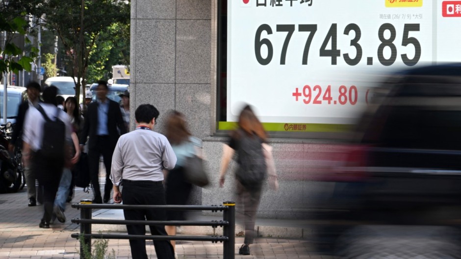 Pedestrians pass by a stock price indicator flashing its closing rate. AFP/Toshifumi Kitamura
