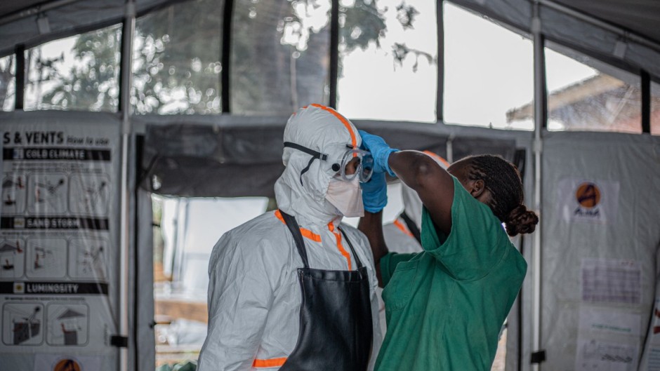 A hygiene worker helps a doctor put on personal protective equipment (PPE) before entering the Rwampara Ebola Treatment Centre. AFP/Benediction Murhabazi