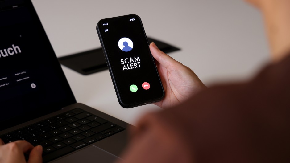A person holds a smartphone displaying a “Scam Alert” message on an incoming call screen. GettyImages/tolgart