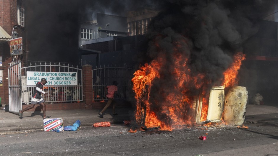 Protesters take cover past a burning car after clashes erupted between protesters and foreign nationals in Durban on October 8, 2026.