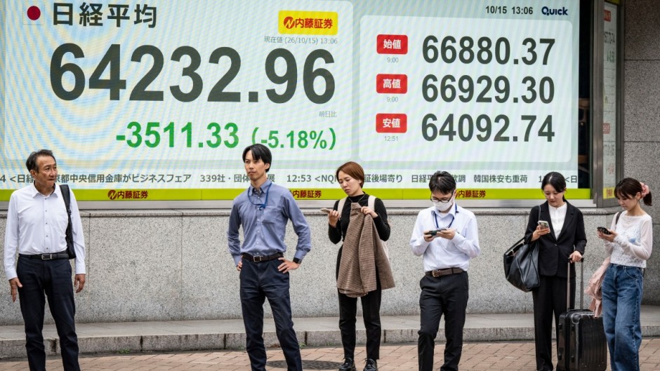 People wait to cross a street in front of an electronic quotation board displaying the Nikkei Stock Average on the Tokyo Stock Exchange. AFP/Yuichi Yamazaki