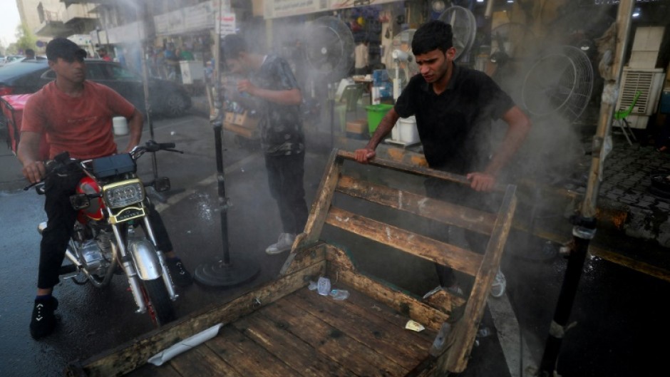 Men cool off with a mist dispenser set up in a street in central Baghdad amid soaring temperatures