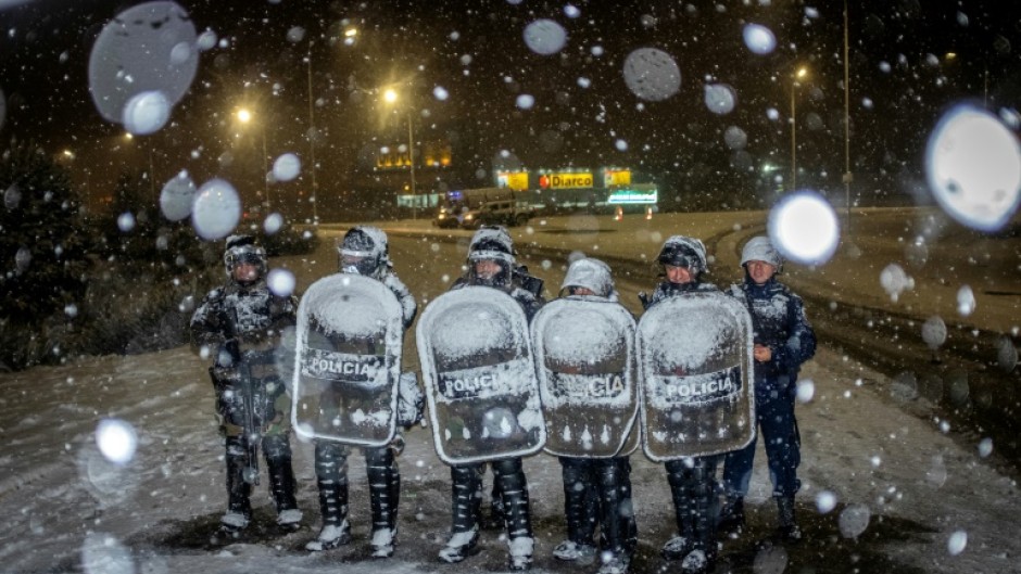 Police officers guard a Diarco supermarket under falling snow after an attempted looting