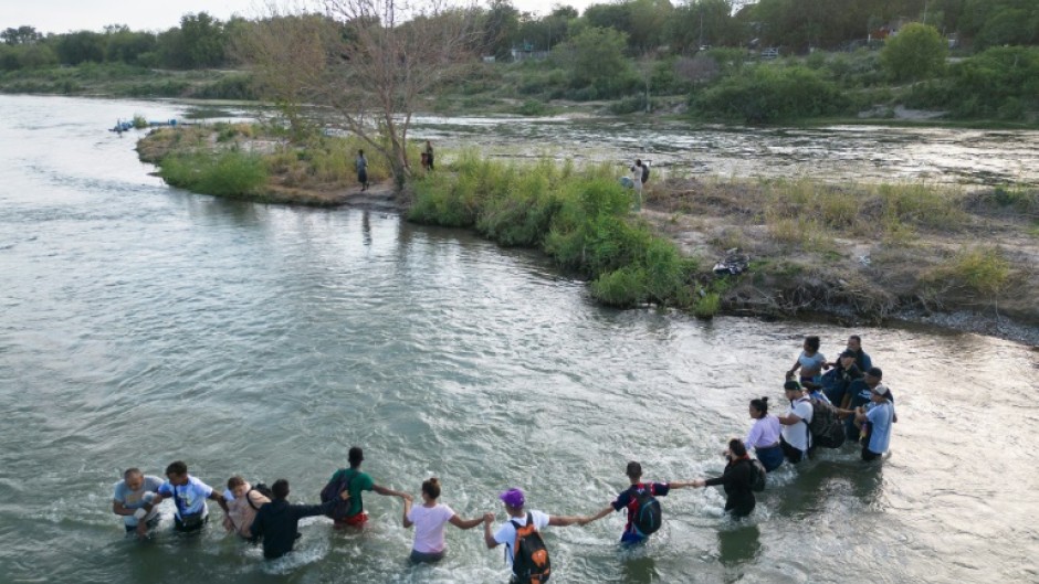 A group of migrants hold hands as they cross the Rio Grande river