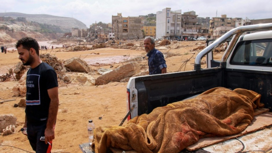 People walk past the body of a victim from the flood which devastated Derna, eastern Libya