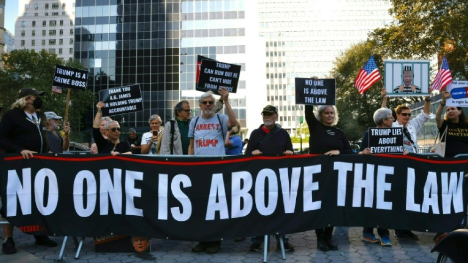 Protestors hold banners outside New York State Supreme Court ahead of the start of a civil fraud trial against Donald Trump
