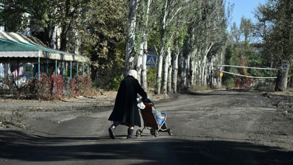 An elderly woman carries bottles of water in a child stroller down a street in the frontline town of Chasiv Yar in eastern Ukraine