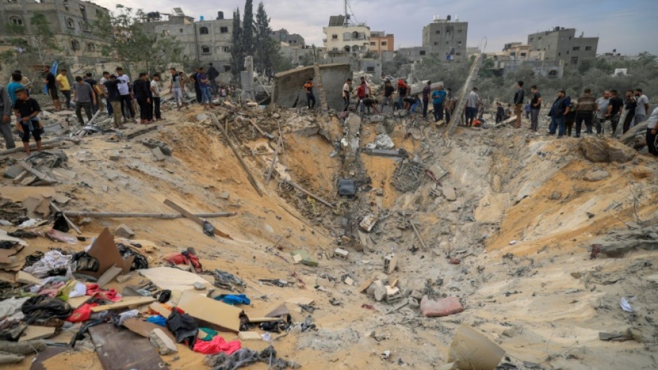People stand over a crater following Israeli bombardment in the southern Gaza Strip 