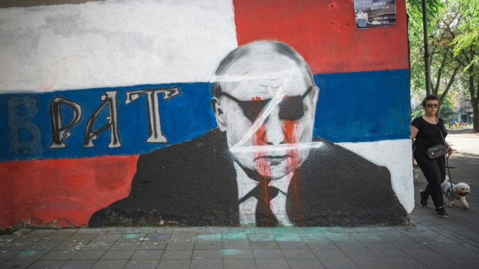 A woman walks past a vandalised mural of Russian President Vladimir Putin in Belgrade